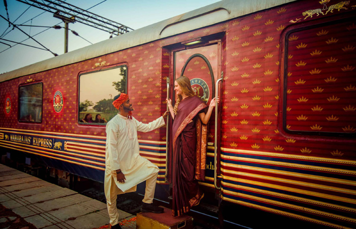 Woman boarding the luxurious Maharaja Express train with a traditional Indian attendant's assistance.