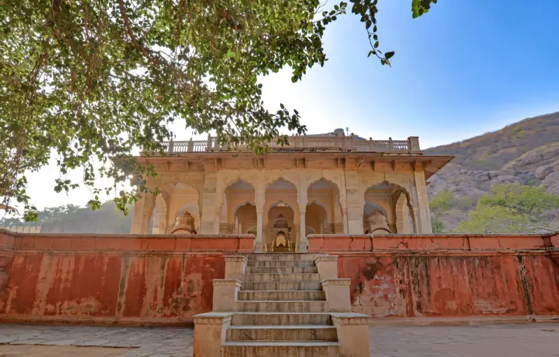 Historic Indian palace surrounded by lush mountains and traditional architecture, with grand stairs leading up to arched doorways.