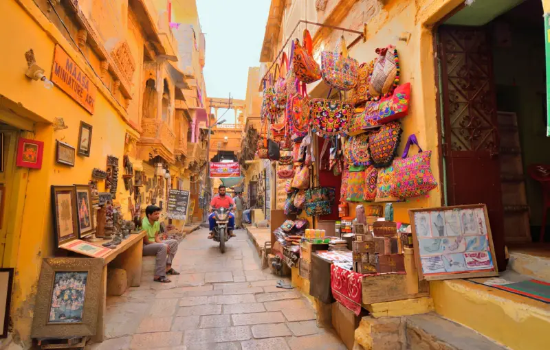 A vibrant Indian marketplace with colorful embroidered bags, traditional art pieces, and street vendors, showcasing the rich culture and crafts of India.